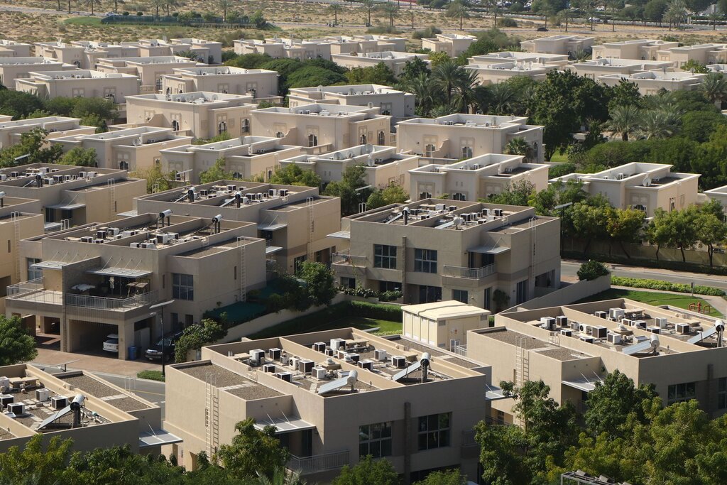 Beige two-storey villas and townhouses with balconies, rooftop air-conditioning units and palm trees in a Dubai community