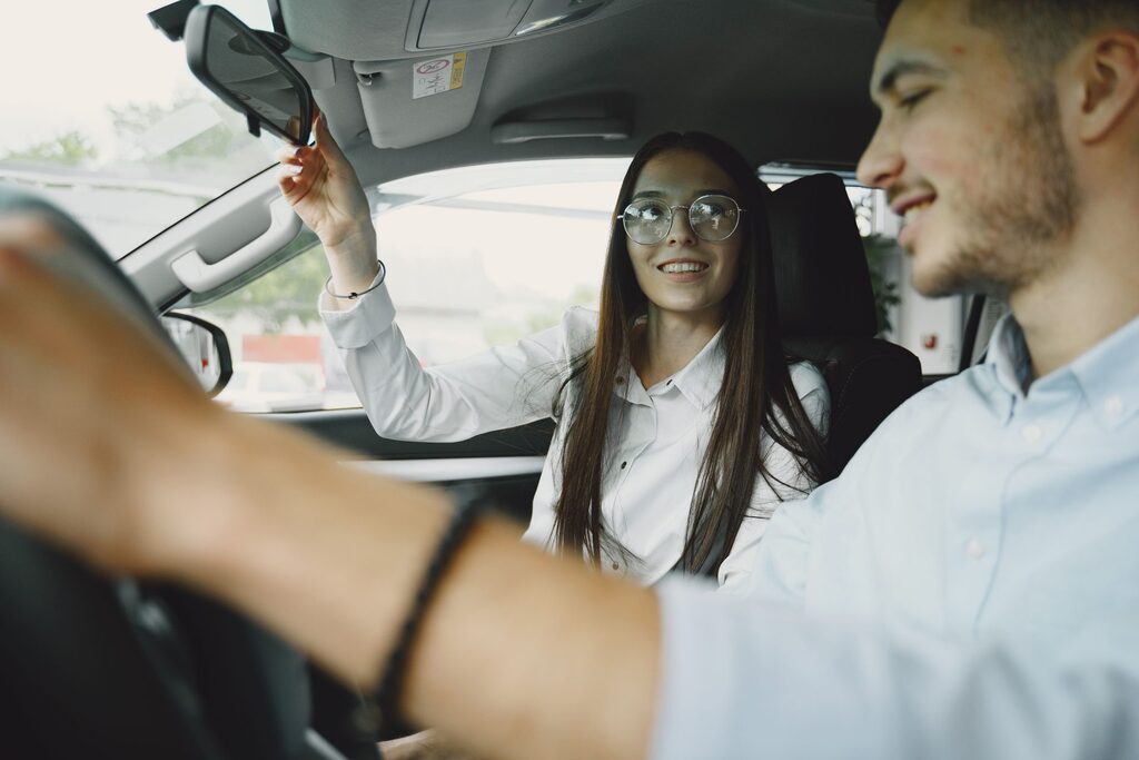 A driving instructor and a learner in a car, the passenger adjusting the rear-view mirror