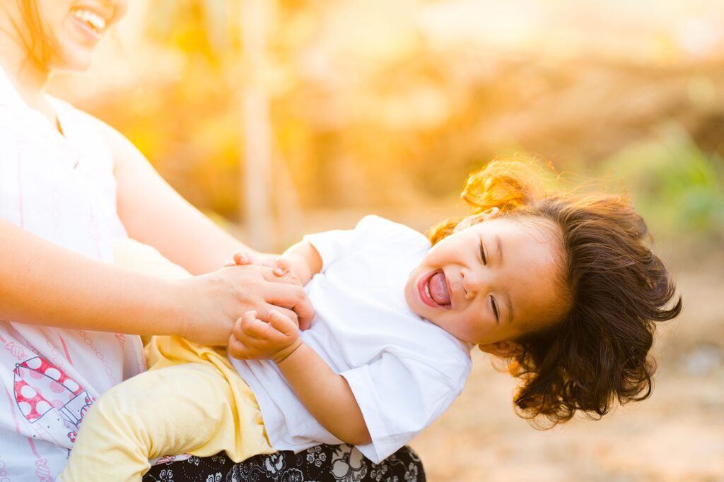 A mother holding a laughing young child outdoors in warm afternoon light